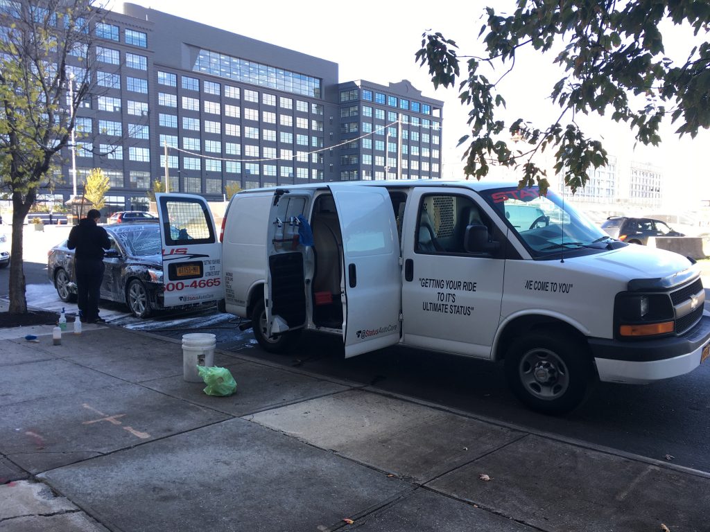 picture of a carwash van washing a car parked next to industry city.